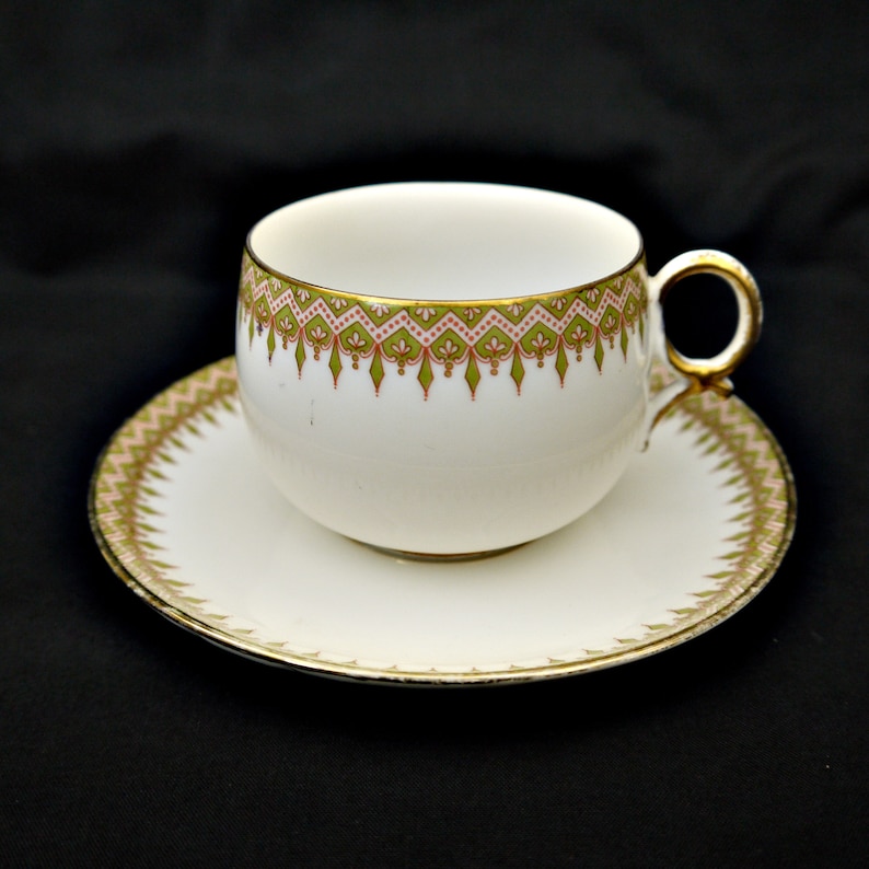 Puede incluir: Una taza de t&eacute; y un platillo blancos con un patr&oacute;n floral verde y rosa y un borde dorado.