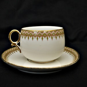 Puede incluir: Una taza de t&eacute; y un platillo blancos con un borde dorado y un patr&oacute;n floral verde y rosa.