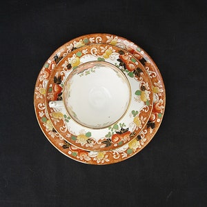 May include: A white teacup with a floral pattern sits on a saucer with a similar floral pattern. The saucer has a brown background with orange, red, and yellow flowers.