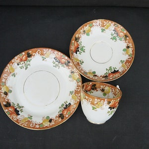 May include: A vintage teacup and saucer set with a floral pattern in shades of orange, brown, and green. The set features a delicate gold trim.