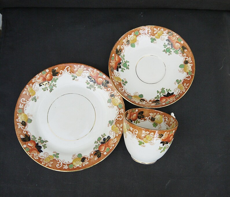 May include: A vintage teacup and saucer set with a floral pattern in shades of orange, brown, and green. The set features a delicate gold trim.