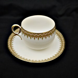 Puede incluir: Una taza de t&eacute; y un platillo blancos con un borde dorado y un patr&oacute;n floral verde y rosa.
