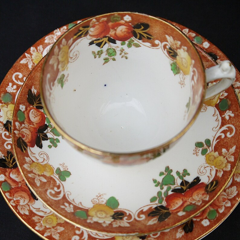 May include: A vintage teacup and saucer set with a floral pattern in shades of orange, green, and black. The set features a gold trim and a white background.