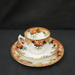 May include: A vintage teacup and saucer set with a floral pattern in shades of orange, brown, and green. The set features a delicate gold trim.