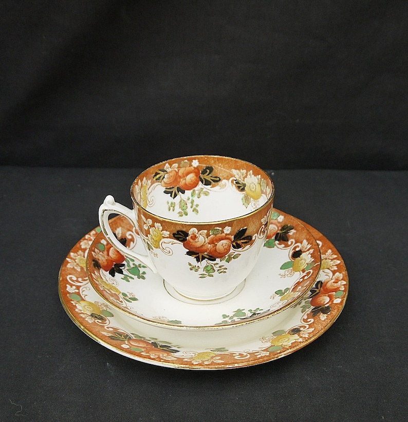 May include: A vintage teacup and saucer set with a floral pattern in shades of orange, brown, and green. The set features a delicate gold trim.