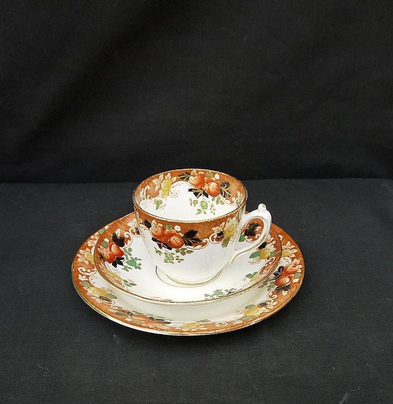 May include: A white teacup and saucer set with a floral pattern in shades of orange, green, and yellow. The cup and saucer have a gold trim.