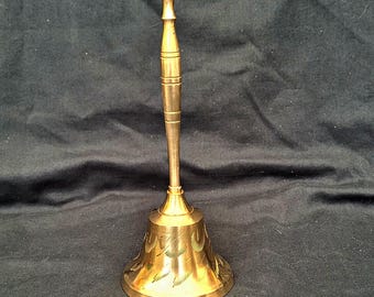 May include: A gold-colored brass bell with an ornate design. The bell has a long handle and a wide, flared base.