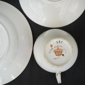 May include: Close-up of the bottom of a white teacup with a brown and red Royal Albion China England mark. The mark includes a crown and the number 451.