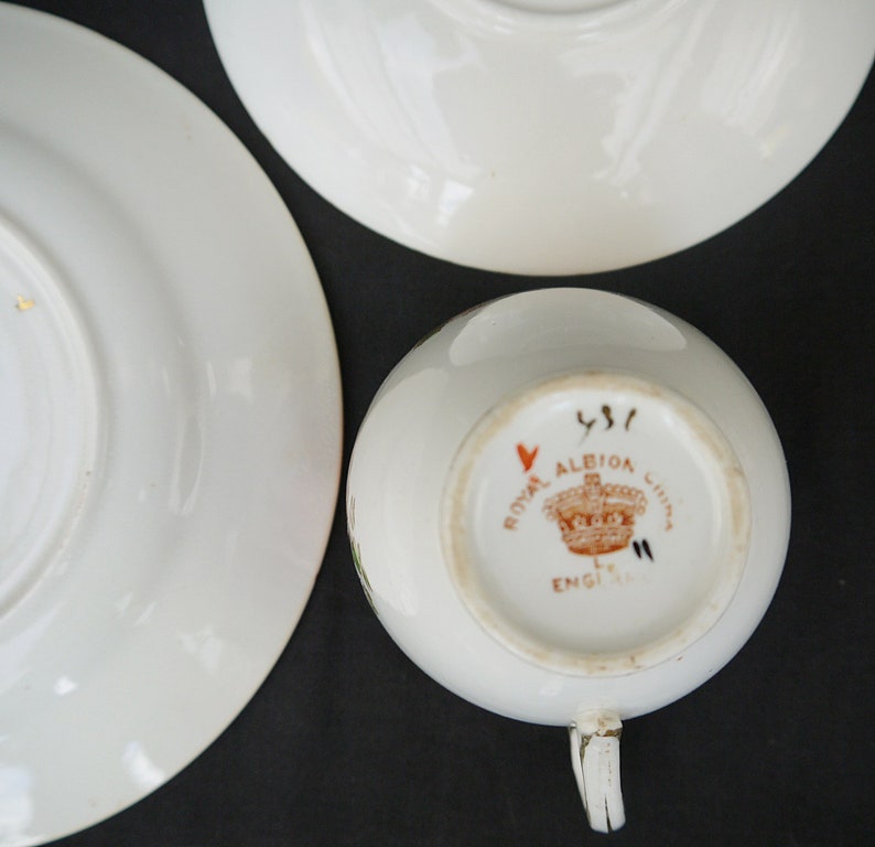 May include: Close-up of the bottom of a white teacup with a brown and red Royal Albion China England mark. The mark includes a crown and the number 451.