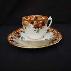 May include: A vintage teacup and saucer set with a floral pattern in shades of orange, brown, and green. The cup and saucer have a gold trim.