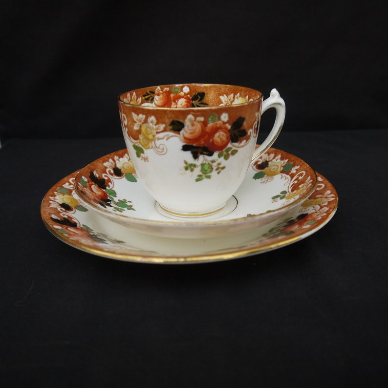 May include: A vintage teacup and saucer set with a floral pattern in shades of orange, brown, and green. The cup and saucer have a gold trim.