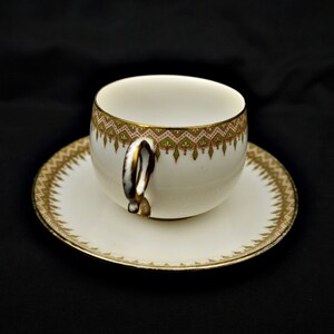 Puede incluir: Una taza de t&eacute; y un platillo blancos con un patr&oacute;n floral verde y rosa alrededor del borde. La taza tiene un asa &uacute;nica.