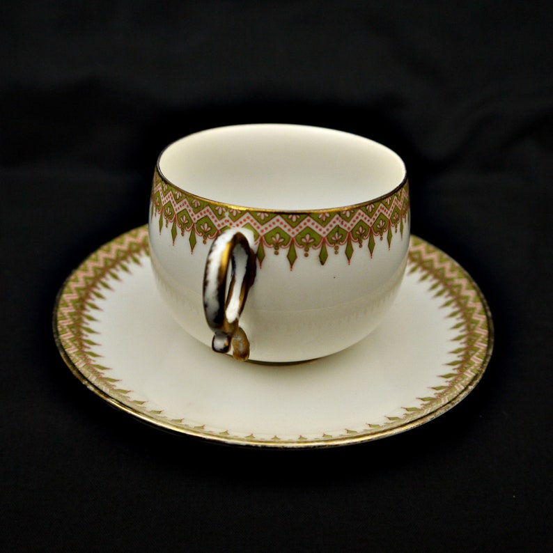 Puede incluir: Una taza de t&eacute; y un platillo blancos con un patr&oacute;n floral verde y rosa alrededor del borde. La taza tiene un asa &uacute;nica.