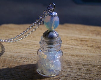 May include: A silver chain necklace with a small glass bottle pendant filled with iridescent white crystals. The bottle has a silver lid and a silver bead with an iridescent blue and white finish.