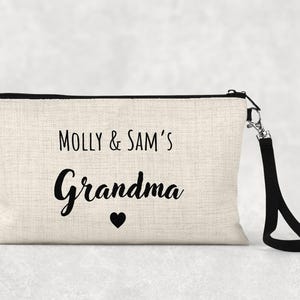 Peut inclure: Une trousse de maquillage en toile beige avec le texte "Molly & Sam's Grandma" en écriture noire. Un cœur noir est en dessous du mot "Grandma". Le sac a une fermeture éclair noire et une dragonne noire.