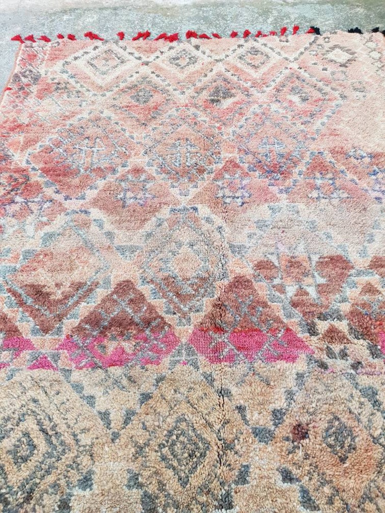May include: A vintage Moroccan rug with a geometric pattern in shades of pink, brown, and gray. The rug has a fringe border.