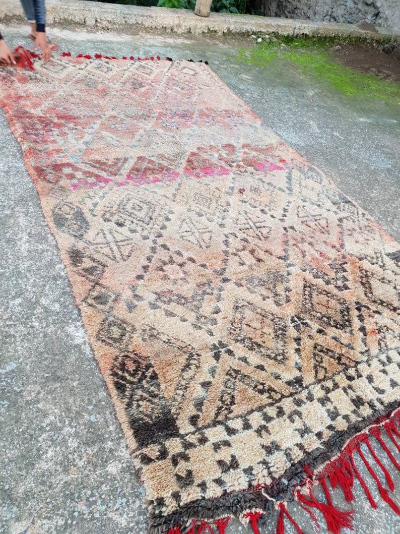 May include: A vintage Moroccan rug with a geometric pattern in shades of brown, beige, and red. The rug has a fringe border and is made of wool.