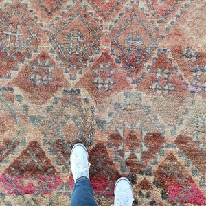 May include: A close-up of a colorful rug with a geometric pattern. Two white sneakers are standing on the rug.