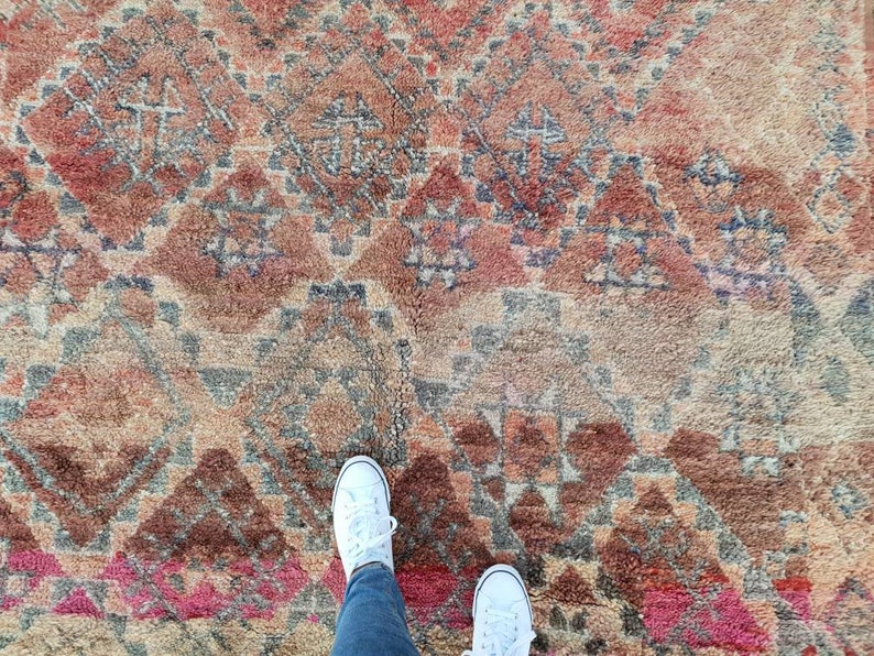 May include: A close-up of a colorful rug with a geometric pattern. Two white sneakers are standing on the rug.