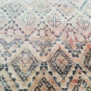 May include: A close-up of a beige and brown rug with a geometric pattern. The rug has a distressed look and is made of wool.