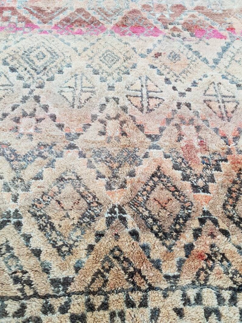 May include: A close-up of a beige and brown rug with a geometric pattern. The rug has a distressed look and is made of wool.