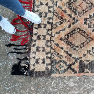 May include: A beige and brown rug with a geometric pattern and red and black fringe. The rug is on a concrete floor.