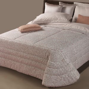 May include: A white and cream floral patterned duvet cover with a white and cream patterned pillow and a peach colored pillow on a bed.