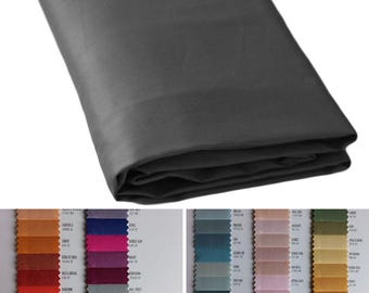 May include: A folded piece of dark charcoal gray fabric with a smooth, matte finish. Below the fabric, two vertical columns display a variety of small, rectangular fabric swatches in numerous colors, each labeled with a name and code.