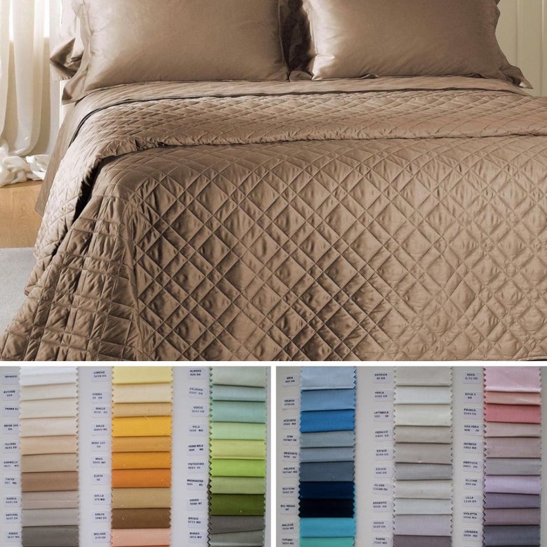 May include: A solid brown quilted bedspread with a diamond pattern, paired with two matching pillow shams. Below the bedspread, two fabric sample boards display a wide variety of color swatches, each labeled with small white text tags.