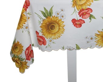 May include: A white rectangular tablecloth featuring a repeating floral pattern of yellow sunflowers, red poppies, and small white daisies. The fabric has a scalloped edge finish along the bottom border, draping over the corner of a table.