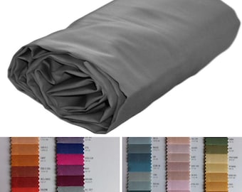 May include: A roll of solid gray fabric with a smooth, matte texture. Below the fabric roll, two side-by-side color swatch charts display a wide variety of fabric samples in various hues, each labeled with its specific color name and code.