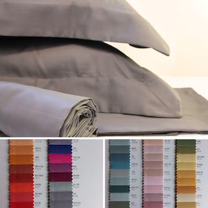 May include: A close-up of a gray fabric swatch with a variety of color swatches in the background. The color swatches are arranged in rows and columns, and they include a variety of colors, including red, orange, yellow, green, blue, purple, and brown.