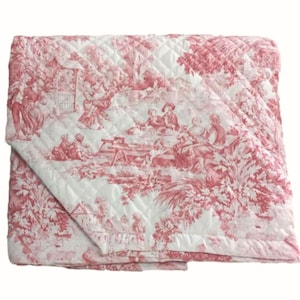 Op de afbeelding: Een witte doorgestikte deken met een rood toile de jouy patroon. Het ontwerp toont diverse figuren in scènes buitenshuis, waaronder mensen aan tafels, bomen en gebladerte, alles uitgevoerd in een gedetailleerde, herhalende monochrome print.
