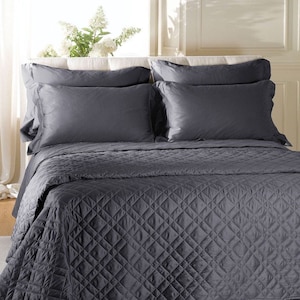 May include: A dark gray bedding set featuring a quilted coverlet with a diamond-stitched pattern and four matching rectangular pillowcases. The bedding is arranged neatly on a bed, showcasing a smooth, uniform dark gray color throughout the set.
