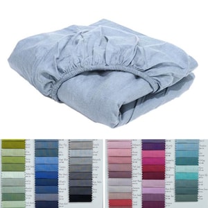 Puede incluir: Una sábana bajera ajustable azul claro doblada con bordes elásticos. La sábana está hecha de una tela suave y se muestra sobre un fondo blanco. Las muestras de color son visibles en la parte inferior de la imagen.
