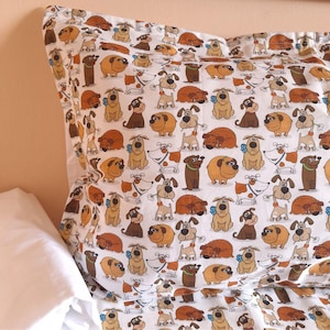 May include: White pillowcase with a repeating pattern of cartoon dogs in various poses and colors, including brown, tan, and white. The dogs have different expressions and are wearing collars. The pillowcase is on a bed.