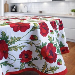 Puede incluir: Un mantel redondo con fondo blanco y un patrón repetitivo de amapolas rojas vibrantes y follaje verde. La tela está rematada con un borde rojo sólido a lo largo del dobladillo inferior, cubriendo los lados de una mesa circular.