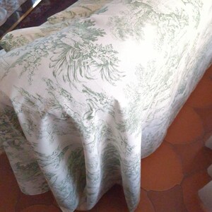 Puede incluir: Una funda de sof&aacute; con base de tela blanca y un patr&oacute;n repetitivo de toile en color verde salvia que representa escenas pastorales, &aacute;rboles y follaje. El tejido cubre el brazo y el asiento del mueble, mostrando el estampado detallado.