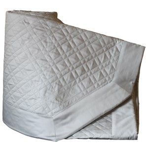 May include: A folded off-white quilt featuring a diamond-shaped quilted pattern across the center panel. The quilt has a smooth, non-quilted border along the edges, creating a clean and structured appearance for this bedding item.