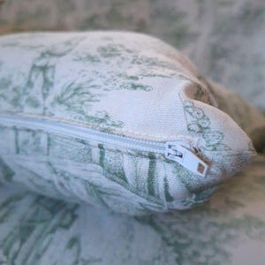 Puede incluir: Una funda de coj&iacute;n rectangular con base de tela blanca y un patr&oacute;n toile de jouy verde que representa escenas pastorales. La funda incluye una cremallera de pl&aacute;stico blanco en el lateral, lo que permite un f&aacute;cil acceso al interior.