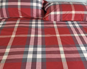 May include: A bedding set featuring a red, white, black, and gray plaid pattern. The set includes a large comforter and two rectangular pillows, all matching in the same tartan-inspired check design with clean, straight lines and a smooth fabric finish.