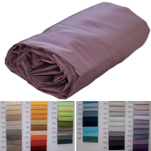 Peut inclure: Un drap housse mauve roulé. Le drap est fait d'un tissu doux et lisse. L'image montre également un nuancier avec différentes nuances de tissu.