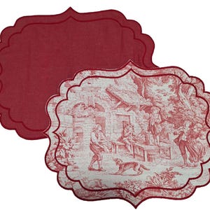 Può includere: Due tovagliette all'americana in tessuto rosso e bianco con bordo a festoni. Le tovagliette presentano un design vintage di un cottage con persone e un cane in un ambiente boschivo.