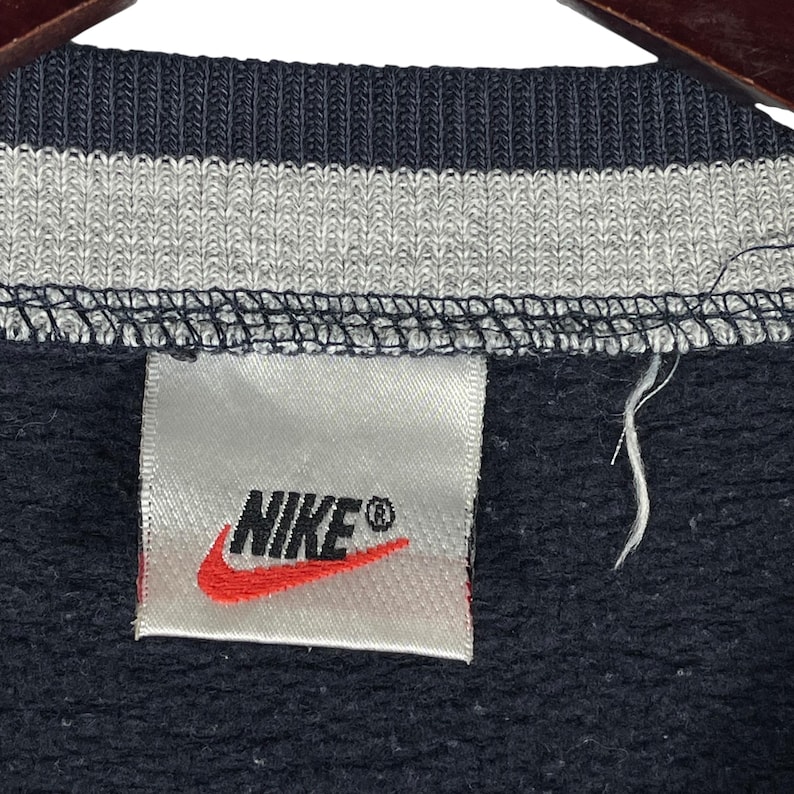 May include: Close-up of a navy blue sweatshirt collar with a gray and white striped design. The Nike logo is visible on a white tag with a red swoosh.