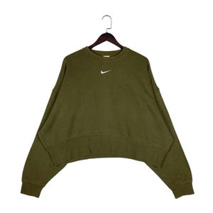 Op de afbeelding: Olijfgroene sweatshirt met een wit Nike-logo. De crewneck sweatshirt heeft een relaxte pasvorm en lange mouwen. Het kledingstuk hangt aan een houten hanger tegen een witte achtergrond.