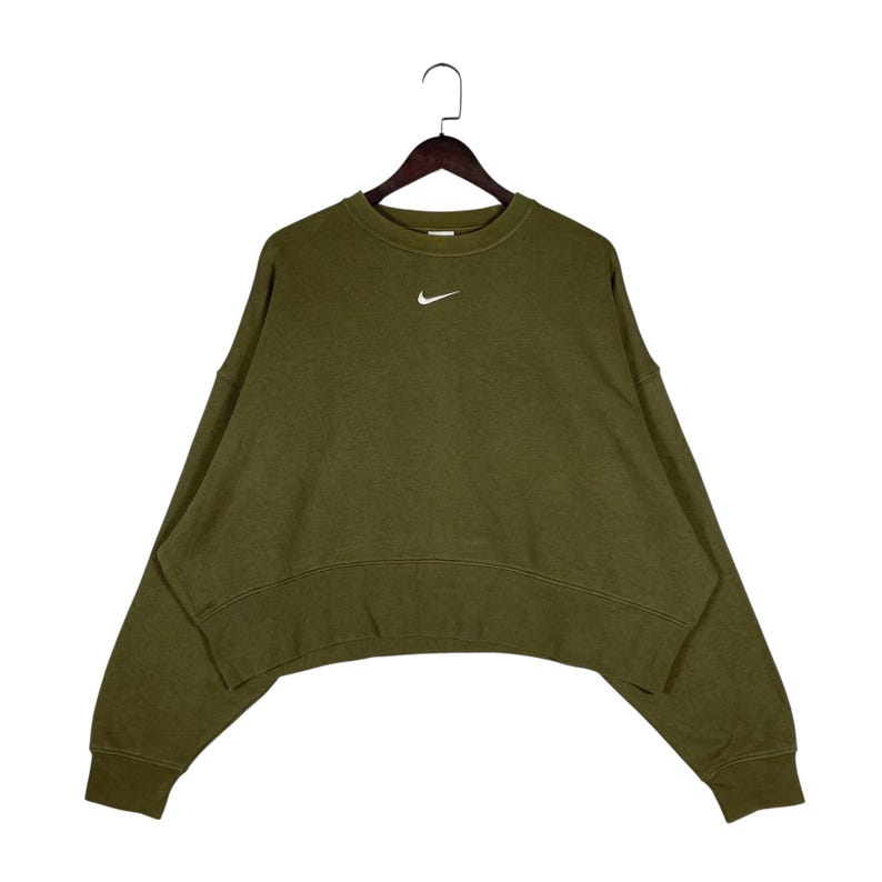 Op de afbeelding: Olijfgroene sweatshirt met een wit Nike-logo. De crewneck sweatshirt heeft een relaxte pasvorm en lange mouwen. Het kledingstuk hangt aan een houten hanger tegen een witte achtergrond.