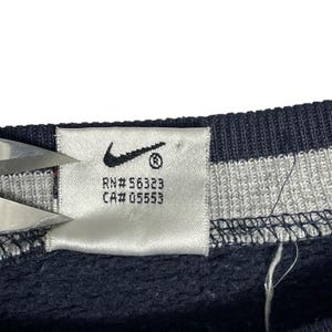 May include: Close-up of a white tag with the Nike swoosh logo and the text "RN# 56323 CA# 05553". The tag is attached to a navy blue garment with white and gray stripes.