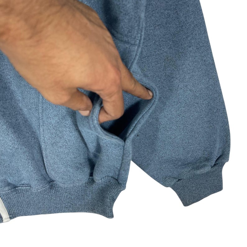 May include: A light blue sweatshirt with a pocket. The sweatshirt has a ribbed hem and cuffs. The fabric appears to be a soft, textured material. The pocket is open, and the garment is clean.