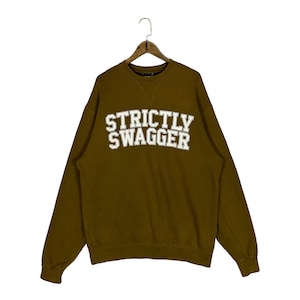 May include: A brown sweatshirt with the text "STRICTLY SWAGGER" in white letters.
