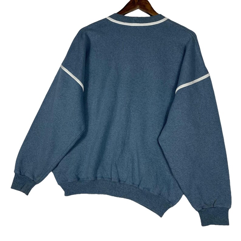 May include: A blue sweatshirt with white trim along the collar and sleeves. The sweatshirt has a crew neck and long sleeves with ribbed cuffs. The garment is hanging on a wooden hanger against a white background.